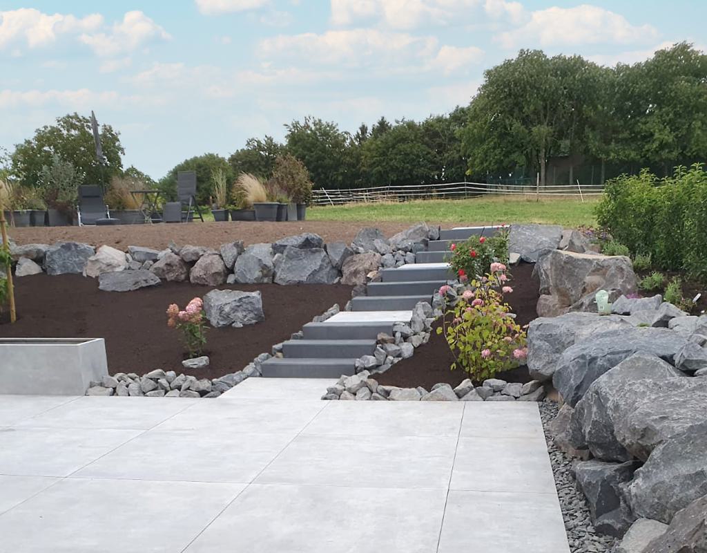 Moderne Gartenanlage mit Betonplatten, Natursteinmauer und integrierter Treppe